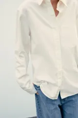 Camisa color crema de corte recto, confeccionada en algodón. Tiene cuello solapa, manga larga con puños abotonados, bolsillo de parche en el pecho y cierre frontal con botones.