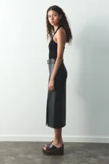 Falda midi negra de cuero sintético, de tiro alto, con cinturón con hebilla metálica y abertura frontal. Cierre lateral con cremallera oculta.