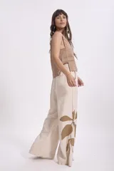 Pantalón ancho de lino color beige claro con estampado grande de hojas en color marrón en la parte inferior de la pierna izquierda. El pantalón tiene un corte holgado y tiro alto.