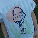 Remera blanca de manga corta con cuello redondo y un estampado central de una medusa en tonos rosados y verdes pastel.
