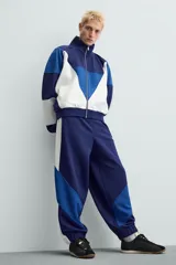 Pantalón deportivo azul marino con paneles laterales blancos y detalles en azul eléctrico. Corte relaxed fit, cintura elástica ajustable con cordón, bolsillos frontales ocultos y puños elásticos.