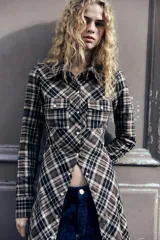 Vestido largo tipo camisero con estampado de cuadros en tonos marrón, negro y blanco. Tiene cuello solapa, mangas largas con puños abotonados, dos bolsillos de parche con solapa en el pecho y cierre frontal con botones a presión.
