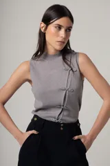 Top gris de tejido de punto, sin mangas, con cuello alto y cierre lateral con botones decorativos.