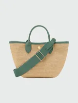 Cartera tipo canasta de tamaño XS confeccionada en tejido de paja con detalles en cuero verde. Presenta dos asas de mano, un parche frontal con el logo de la marca grabado y un dije colgante con cuentas de cerámica. Posee cierre de botón a presión.