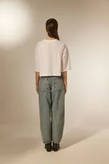 Pantalón jean color blanco, de corte barrel y tiro bajo, con detalles de tachas metálicas en los bolsillos delanteros y a lo largo de las costuras laterales.