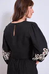 Blusa negra con cuello redondo y mangas largas abullonadas, con apliques bordados de hojas en color crudo en el frente y en las mangas.