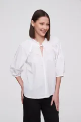 Blusa blanca de algodón con escote en V con lazos, mangas 3/4 abullonadas y corte holgado.