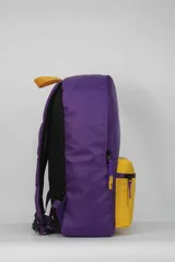 Mochila de nylon con diseño bicolor, cuerpo principal morado y bolsillo frontal amarillo. Presenta el logo de Los Angeles Lakers en el frente y un pequeño logo de la NBA en la parte inferior derecha. La espalda está confeccionada con tela mesh.