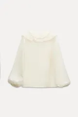 Camisa color crudo confeccionada en tejido de lyocell, con escote en pico, mangas largas abullonadas con elástico en los puños y volantes frontales.