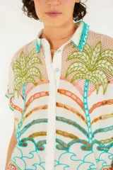 Camisa blanca con estampado de motivos playeros en tonos verdes, marrones, celestes y rosados. Tiene cuello clásico, cierre con botones y mangas cortas.