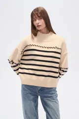 Sweater beige con rayas horizontales negras, cuello alto y corte holgado.