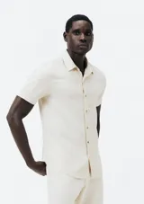 Camisa de lino color crema, de corte clásico, con cuello camisero, manga corta y bolsillo en el pecho. Cierre frontal con botones.