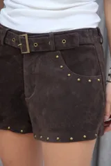 Short de gamuza color marrón oscuro, con tiro alto, cinturón incorporado con hebilla metálica y tachas doradas decorativas en los bordes de los bolsillos y el ruedo.