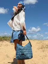 Bolso tipo shopper color beige con diseño acolchado geométrico y correa de hombro negra.