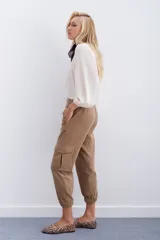 Pantalón de corderoy gris, de corte holgado, con elástico en la cintura, cierre y botón. Tiene bolsillos aplicados en el delantero y puños con elástico interno.