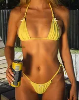 Traje de baño de dos piezas color amarillo, con corpiño triangular con tirantes finos y detalle de lazos en los extremos superiores. La bombacha es tipo colaless con tiras finas a los costados y detalle de lazo en el centro.