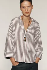 Camisa a rayas verticales color marrón y blanco, de corte holgado, con cuello solapa, cierre frontal con botones y mangas anchas por debajo del codo.