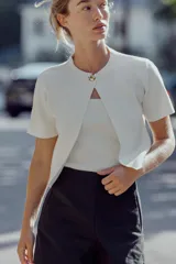 Chaqueta blanca de punto con cuello redondo y manga corta. Cierre frontal con un botón dorado.