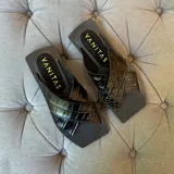 Sandalias negras con tiras anchas cruzadas de cuero con textura tipo cocodrilo y suela plana cuadrada.