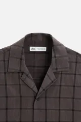 Camisa de hombre color gris con diseño a cuadros, corte relaxed fit, cuello bowling, manga corta y cierre frontal con botones.