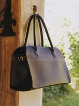 Bolso tipo tote de cuero negro con textura tipo piel de cocodrilo, doble asa de mano y cierre superior con cremallera.