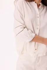 Blusa color blanco de lino liviano con detalle de elástico en el ruedo y recortes calados en las mangas.