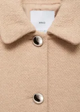 Chaqueta corta color beige de tweed con cuello camisero y cierre frontal con botones metálicos.