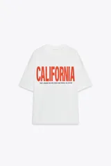 Camiseta blanca de corte amplio con cuello redondo y mangas cortas. Estampado frontal con la palabra "CALIFORNIA" en color rojo y debajo la dirección "7007, FRIARS RD STE 222A SAN DIEGO, CA 92108".