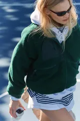 Chaqueta de polar suave y esponjosa color verde oscuro, con cierre a presión frontal, bolsillos con cremallera y parches de nailon. Tiene una silueta ligeramente oversize y llega justo por debajo de la cintura.