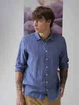 Camisa azul de lino con botones blancos, manga larga y bolsillo en el pecho.
