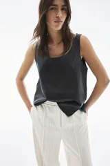 Pantalón de sarga color crudo con finas rayas verticales en gris, de tiro alto con cintura elástica y cierre decorativo. Tiene bolsillos laterales discretos y piernas anchas con pliegues cosidos adelante y pliegues planchados atrás.
