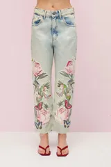 Pantalón de jean celeste con lavado vintage y calce mom. Presenta parches bordados con motivos florales, de mariposas y colibríes. El ruedo está desflecado.