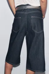 Bermuda de jean azul oscuro, tiro medio, con cinco bolsillos, trabillas en la cintura y pespuntes marcados a contraste.