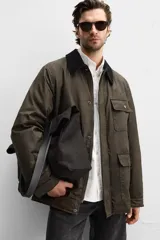 Parka relaxed fit color verde oscuro confeccionada en tejido de algodón con acabado encerado. Tiene cuello solapa combinado en pana negra, manga larga acabada en puño ajustable con botón a presión, bolsillos frontales de plastrón con solapa, bolsillo interior y cierre frontal de botonadura oculta por solapa.