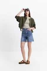Campera corta color verde militar, sin cuello, con cierre frontal y elástico en la cintura. Tiene bolsillos amplios y mangas largas con puños elásticos.