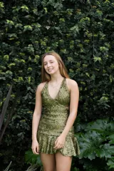 Vestido corto de lentejuelas color verde oliva, con escote en V, breteles finos cruzados en la espalda, cut-outs laterales y volado en el ruedo.