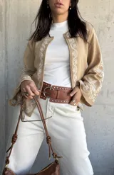 Chaqueta color beige con bordados blancos en el frente y las mangas, de corte recto y mangas anchas.