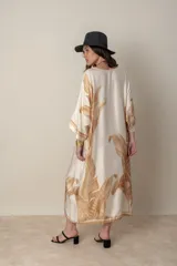 Vestido largo color natural con estampado de hojas de palmera en tonos verdes. Tiene corte amplio tipo túnica, cuello redondo, mangas tres cuartos, bolsillos laterales y ruedo con ribete.