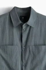 Camisa de manga corta color gris con dos bolsillos frontales con solapa y cierre de botones.