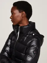 Campera puffer negra de nailon con relleno de plumón, capucha fija con ribete extraíble de pelo sintético, cuello alto, cierre de cremallera, bolsillos laterales con cremallera y parche con el logo de Tommy Hilfiger en la manga.