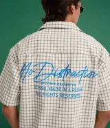 Camisa de hombre de manga corta, cuello inglés y corte boxy, confeccionada en algodón tricolina texturizada a cuadros. Presenta abotonado frontal y bordado en la espalda.