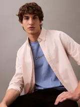 Camisa de manga larga color rosa claro, confeccionada en tejido Oxford de algodón y elastano. Presenta cuello camisero clásico, cierre frontal con botones y logo de Calvin Klein bordado en el pecho. Corte regular.