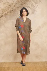 Vestido camisero midi color marrón translúcido, con cuello en V, mangas largas y cierre frontal con botones. Presenta bordados de motivos marinos en tonos rojos, azules y blancos.