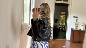 Campera corta de cuero sintético color marrón oscuro, con cuello solapa y detalles de tachas plateadas en el frente, hombros y puños. Presenta mangas amplias.