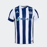 Camiseta de fútbol Le Coq Sportif del Club Atlético Talleres, modelo titular Fan 2025. Diseño a bastones verticales azul marino y blanco, con cuello en V blanco y detalles en azul marino en el borde. Incluye el escudo del club, logo de Le Coq Sportif y sponsors.