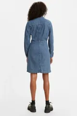 Vestido camisero de denim azul con calce amplio, cuello camisero, mangas largas con puños abotonados, cierre frontal con botones y bolsillos en el pecho.