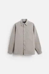 Camisa color gris topo de corte relajado, confeccionada en tejido de mezcla de algodón suave al tacto. Tiene cuello solapa, manga larga con puños abotonados, bolsillo de parche en el pecho y cierre frontal con botones.