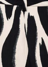 Pantalón largo de viscosa con estampado de cebra en blanco y negro, tiro medio, diseño recto y cierre frontal con botón, gancho y cremallera.