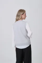 Chaleco de punto color crema, con cuello en V, cierre frontal de botones y dos bolsillos frontales.