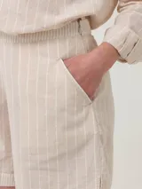 Short de tiro alto color beige con finas rayas verticales blancas. Presenta bolsillos laterales y cierre invisible.